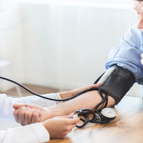 Cardiology. Mexican doctor measuring blood pressure of senior man, checking patient, free space