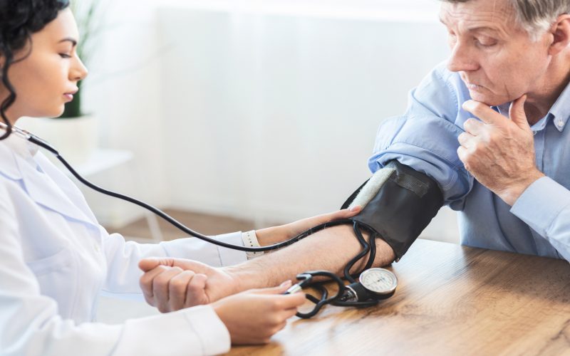 Cardiology. Mexican doctor measuring blood pressure of senior man, checking patient, free space